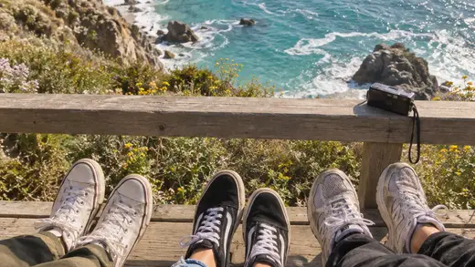 Three friends’ sneakers as they sit together overlooking the blue sea.