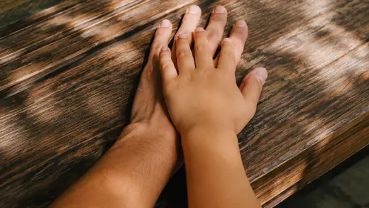 A child's hand resting on an adult's hand on a wooden veranda floor.